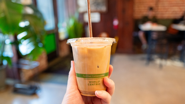 A person holding up an iced latte in a plastic cup at a cafe