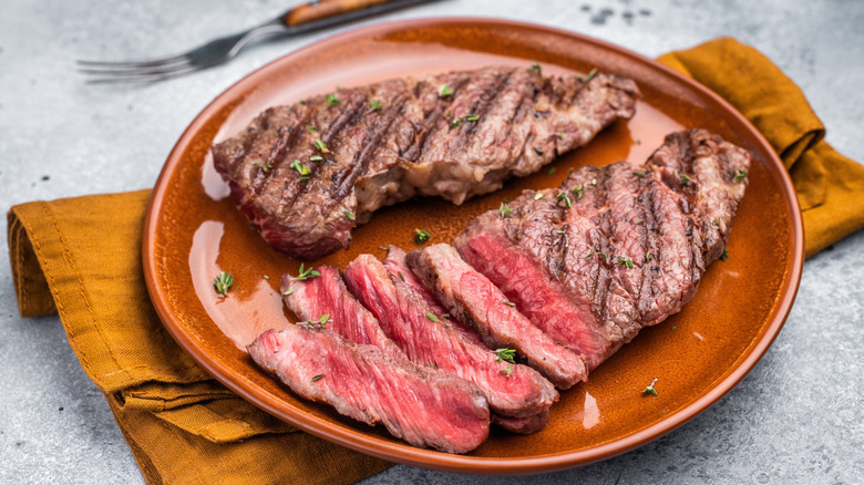 Two tender, juicy flat iron steaks on a brown plate, one of which is sliced and ready to eat