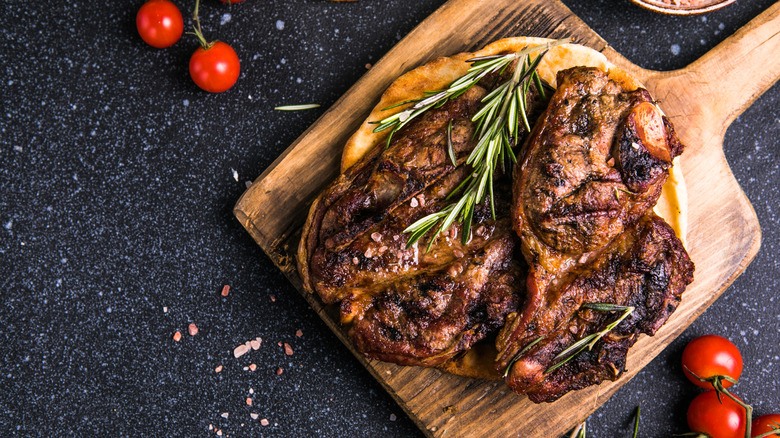 A generously sized porterhouse steak on a wooden cutting board garnished with rosemary and cherry tomatoes