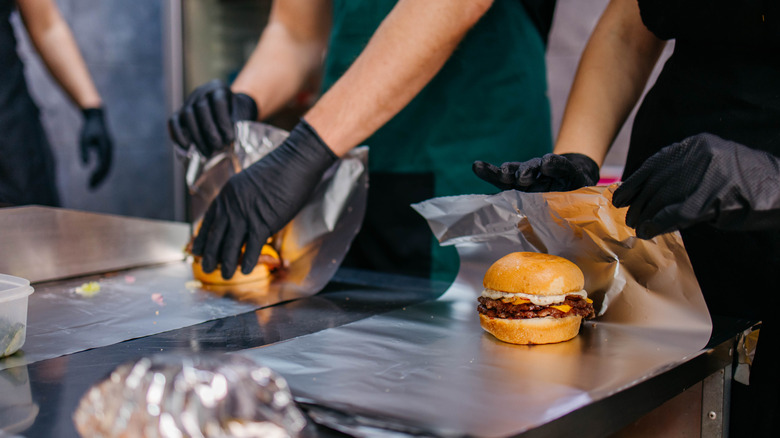 Kitchen staff packing burgers with foil in restaurant