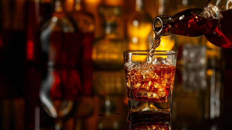 Whiskey being poured from a bottle into a glass sitting on a wooden bar
