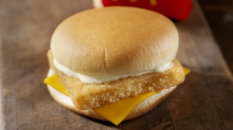 McDonald's Filet-O-Fish Sandwich on a wooden surface with a carton of french fries in the background