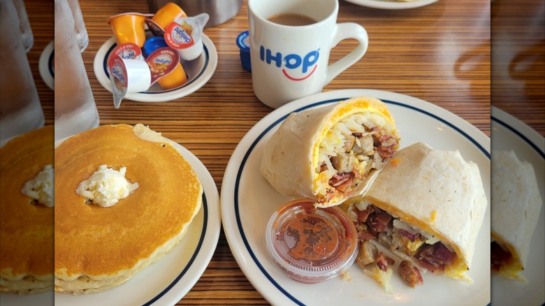 Table inside IHOP restaurant holding logo coffee cup, small bowl of coffee creamer, plate of pancakes, and halved breakfast burrito