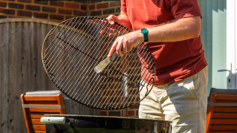 A man stands and scrapes his grill grate