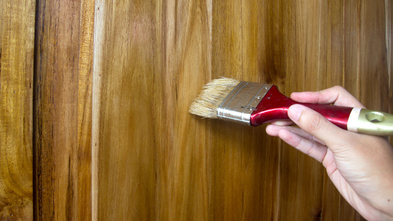 A hand holding a brush against a seemingly oiled wooden surface.