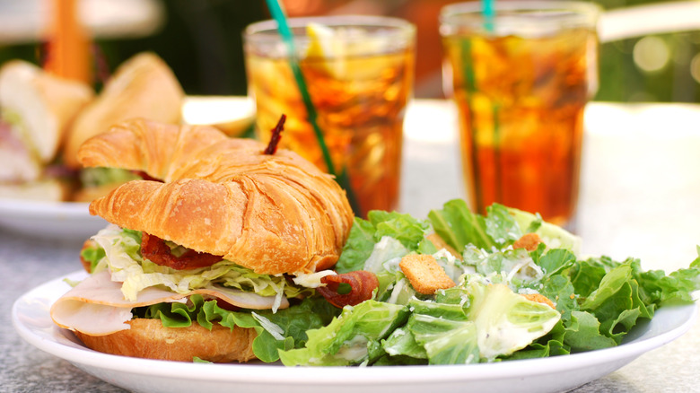 A sandwich and salad sit on a plate beside two drinks on a table.
