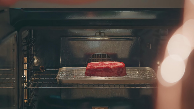 Thick raw steak in the oven on a wire rack above a sheet pan