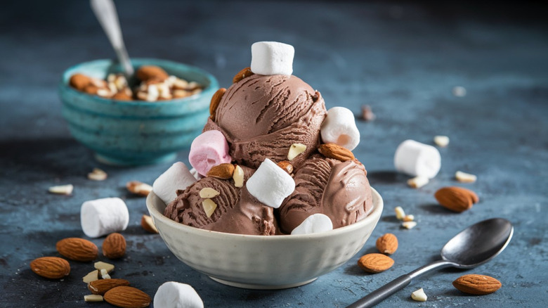Thre scoops of rocky road ice cream in a bowl with marshmallows and almonds scattered
