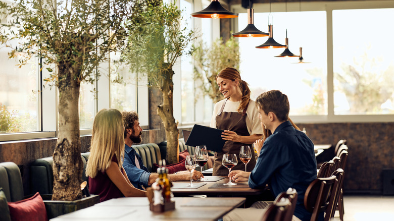 A server taking care of a table of four people each with wine glasses in front of them at a well lit and airy restaurant