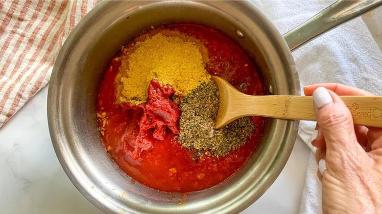 Stirring nutritional yeast into pizza sauce