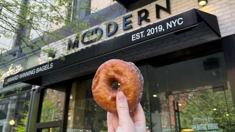glazed donut being held in front of storefront in NYC