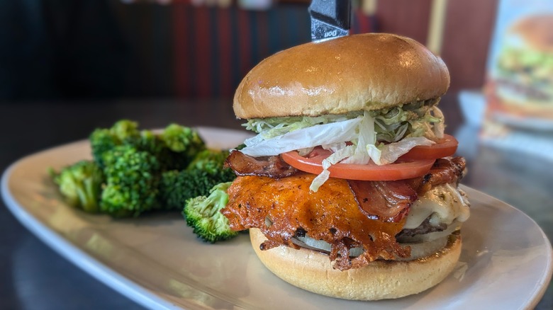 Burger with cheese crisp and bacon and side of broccoli on whtie plate