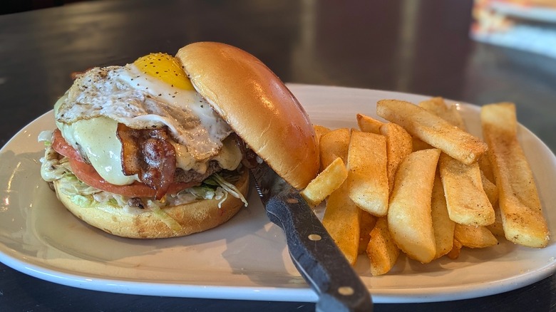 Burger with sunny side-up egg and bacon and side of steak fries on white plate