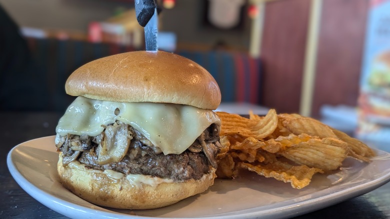 Burger with melted swiss and mushrooms and side of chips on white plate