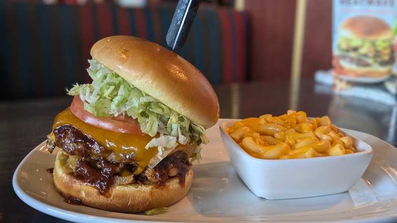 Tall burger with barbeque sauce and side dish of macaroni and cheese on white plate