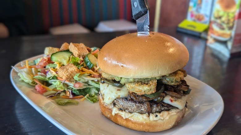 Burger with pepperjack and fried jalapenos with side salad on white plate
