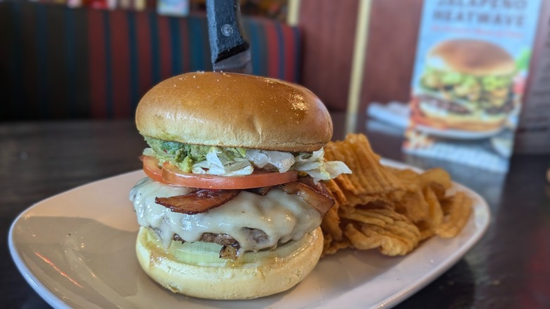 Burger with swiss, bacon, and avocado and chips on the side on white plate