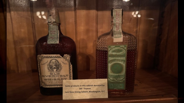Two vintage whiskey bottles in a display case, with a bottle of Old Overholt on the left