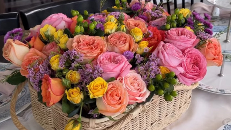 A wicker basket filled with mason jars of pink, purple, and yellow fresh flowers