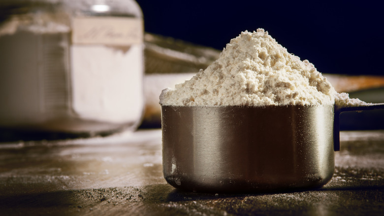 a measuring cup full of flour with a mason jar filled with the same in the background