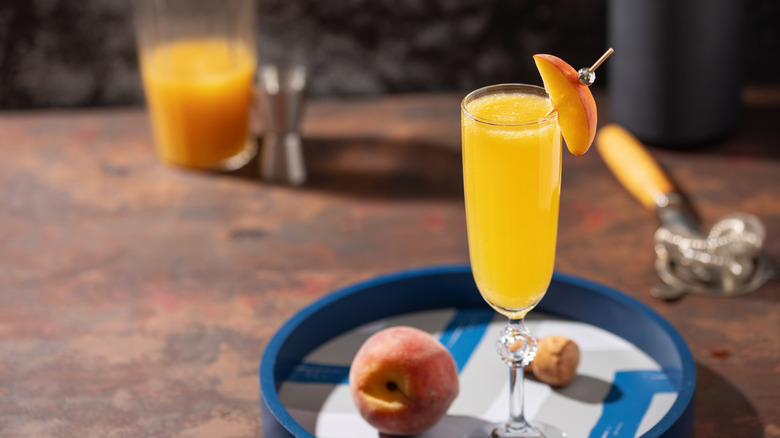 peach bellini outside on tray next to a peach with peach slice garnish