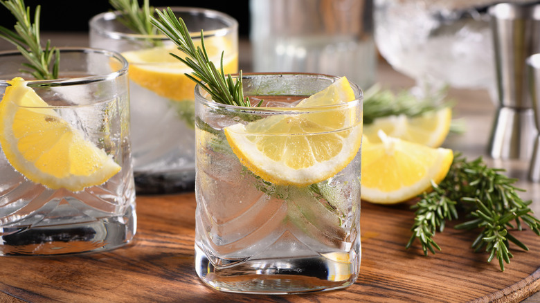 Cold gin and tonic glasses with lemon slice and rosemary sprig on a wooden cutting board.