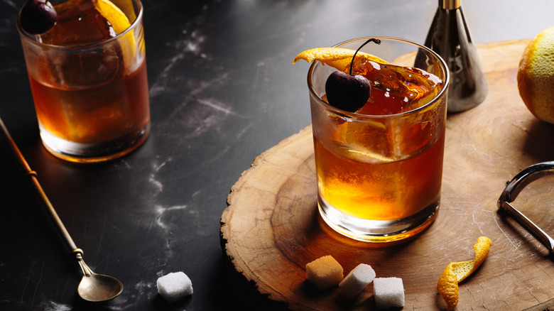 old fashioned cocktail surrounded by ingredients sugar and citrus peel