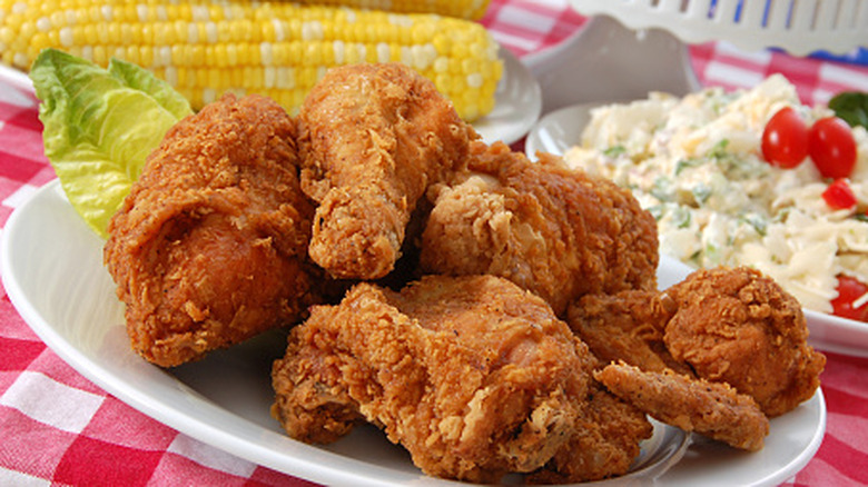 fried chicken on a gingham tablecloth with bow tie macaroni salad and corn on the cob in the background