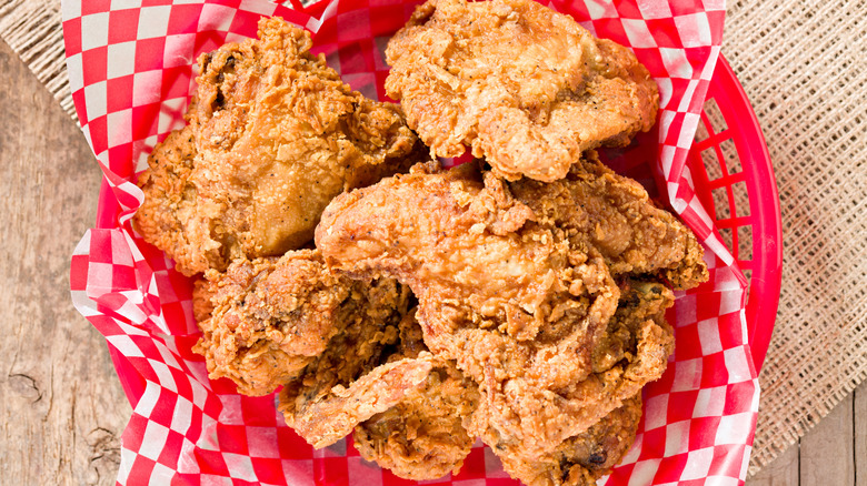 Several pieces of crispy looking Fried Chicken in a red basket on an outdoor wooden table