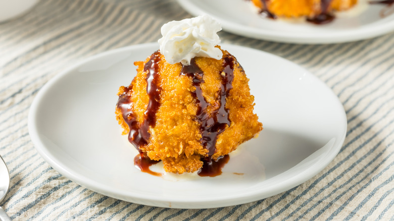 Fried ice cream with chocolate drizzle and whipped cream on white plate