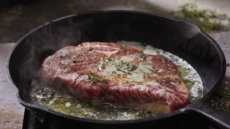 large steak cooking in lots of fat in a cast iron skillet