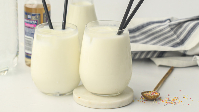 Two glasses of vanilla egg cream with straws and sprinkles nearby
