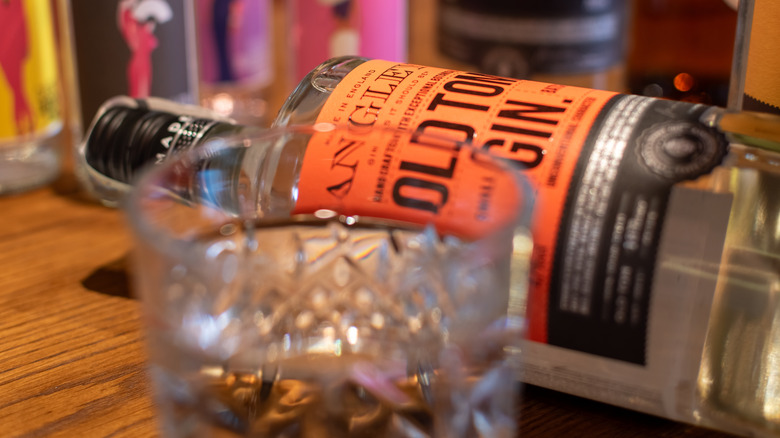 Bottle of Old Tom gin lying on side with rocks glass