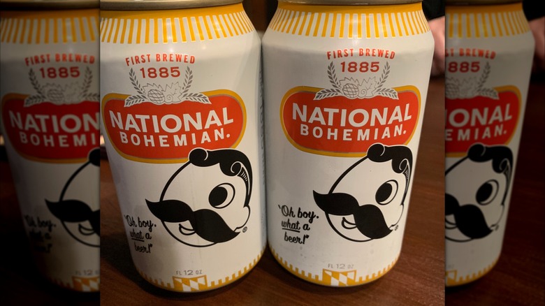 Mirrored image of two unopened cans of National Bohemian on a table