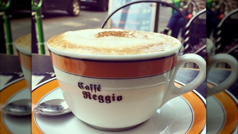 Cappucino cup branded with Caffe Reggio filled with cappuccino on a saucer