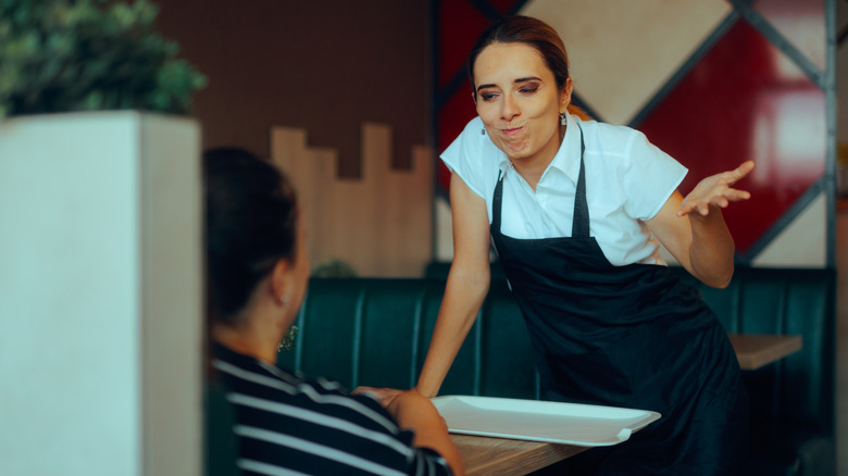 An annoyed waiter gesturing while speaking to restaurant diner