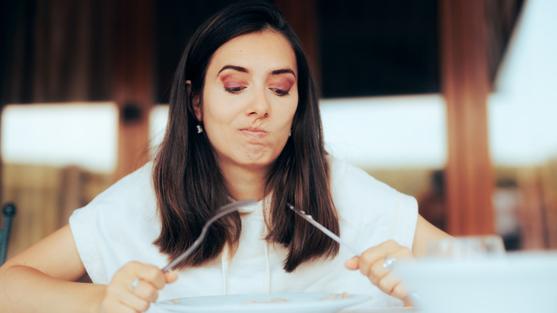 An unhappy woman in a restaurant holding a knife and fork