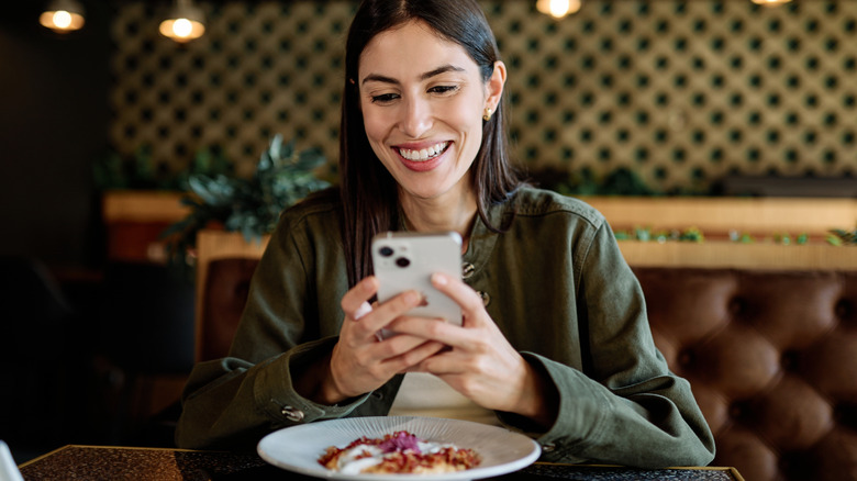 A diner with a plate of food holding her phone up in a restaurant
