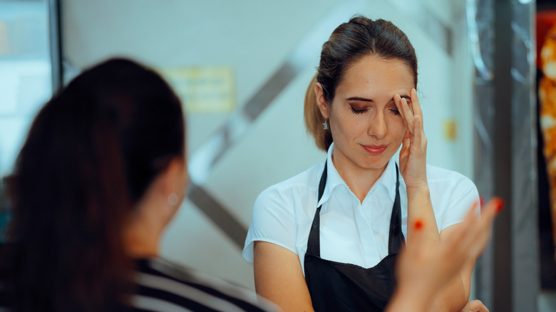 An angry customer gestures at a tired server in a white shirt and black apron