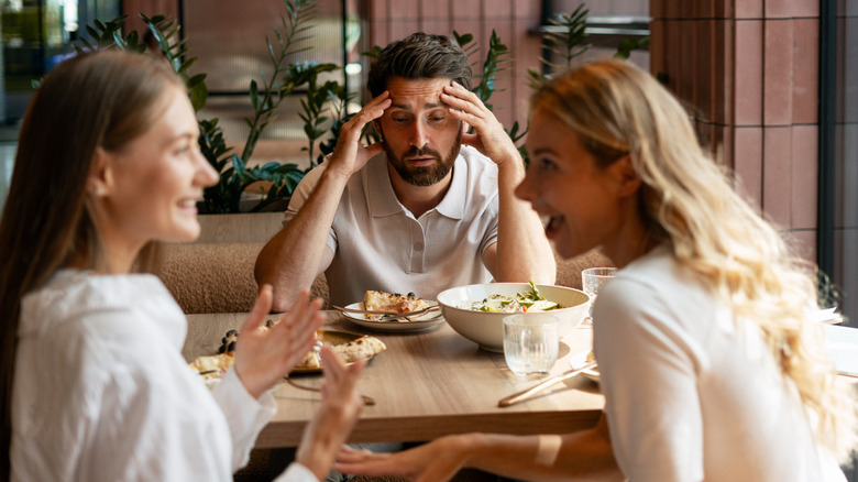 Friends chatting and a man looking bored at restaurant table