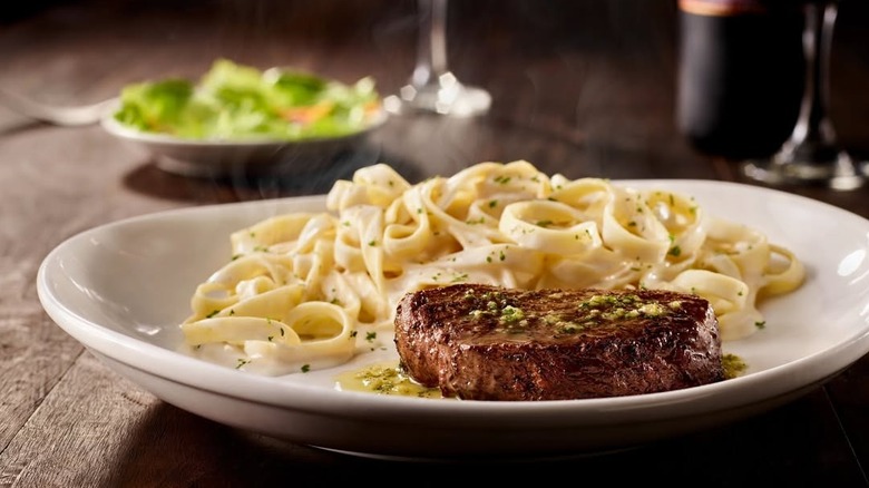 Grilled sirloin steak from Olive Garden served with fettuccine alfredo on white plate