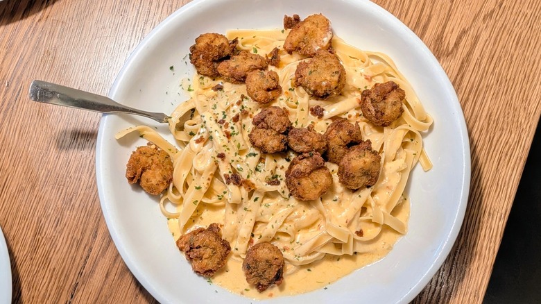 A top view of a bowl of fettucini with Alfredo sauce and small crispy shrimp in a white bowl