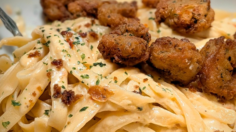A close-up of Alfredo sauce-covered fettucini noodles and small crispy shrimp with herbs
