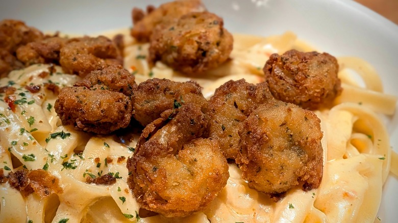 A close-up of crispy shrimp in a bowl of pasta with Alfredo sauce