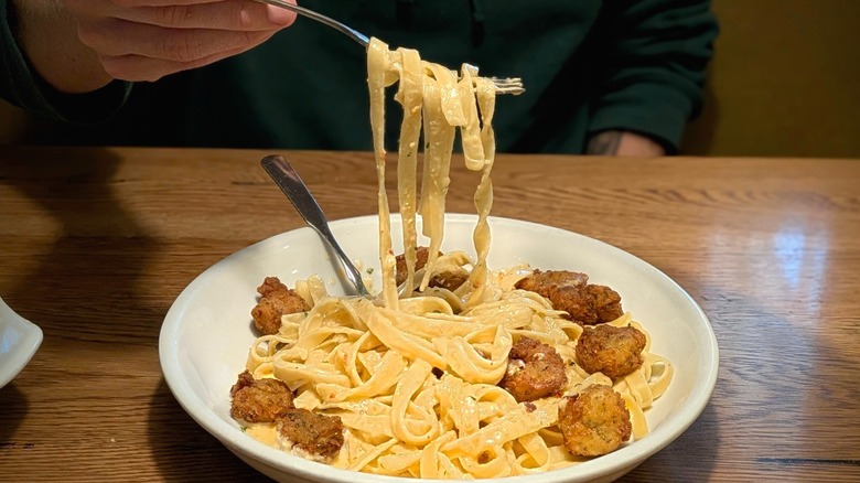 A handing lifting a fork of Alfredo sauce-covered noodles out of a pasta bowl with crispy shrimp