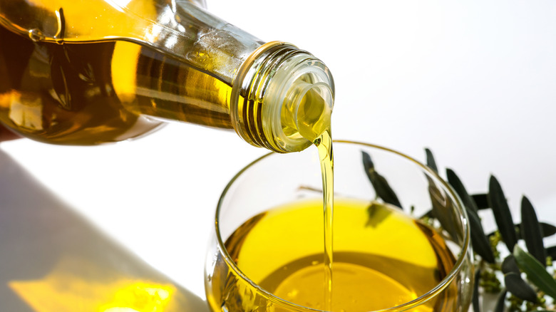 Olive oil being poured from a bottle into a small glass.