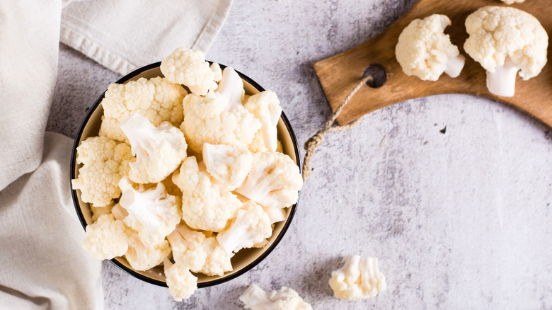 Bowl of raw cauliflower florets next to a cutting board with more florets