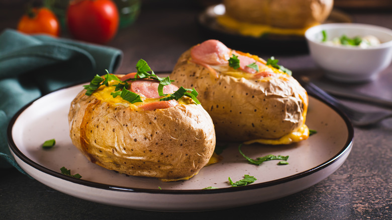 Two twice baked potatoes topped with herbs on white ceramic plate