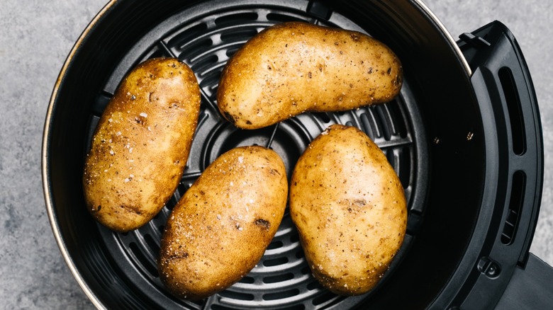 Four whole potatoes with salt inside black air fryer basket