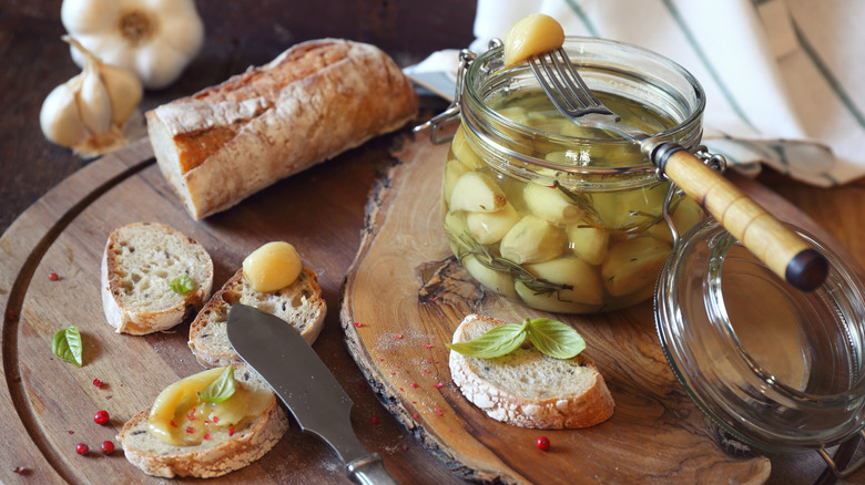 Garlic confit in jar plus rustic bread and garlic spread on one slice all arranged on cutting boards